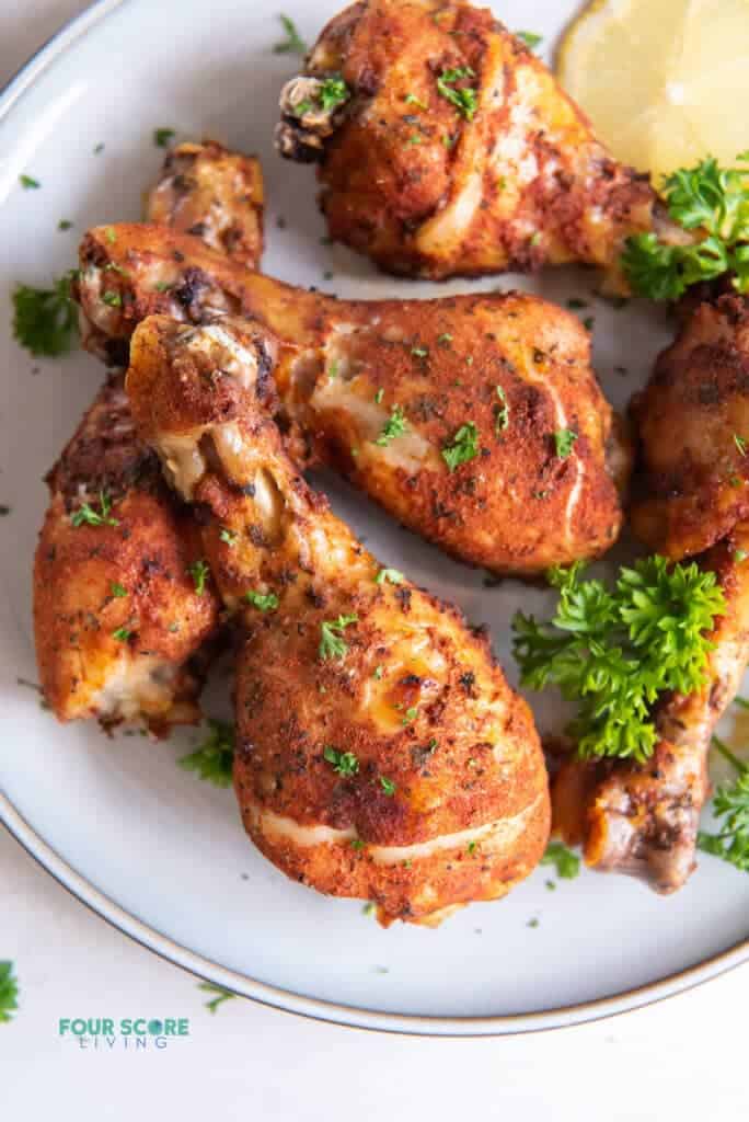 a plate of browned, seasoned chicken legs garnished with fresh parsley.
