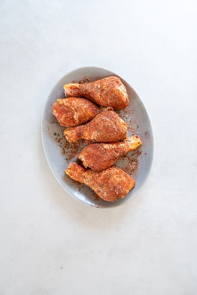 Top view photo of 5 chicken legs on a plate, coated in Instant Pot Chicken Legs seasoning.