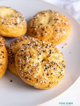 Closeup of a homemade keto bagel with everything seasoning, on a white plate with 5 other bagels