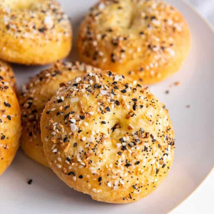Closeup of a homemade keto bagel with everything seasoning, on a white plate with 5 other bagels