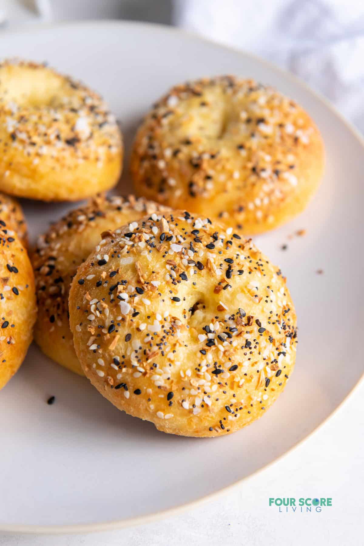 Closeup of a homemade keto bagel with everything seasoning, on a white plate with 5 other bagels