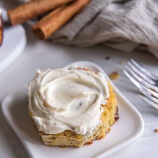 a single frosted keto cinnamon roll on a small plate