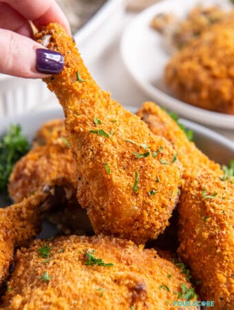 a feminine hand picking up a fried chicken leg from a platter of keto fried chicken pieces