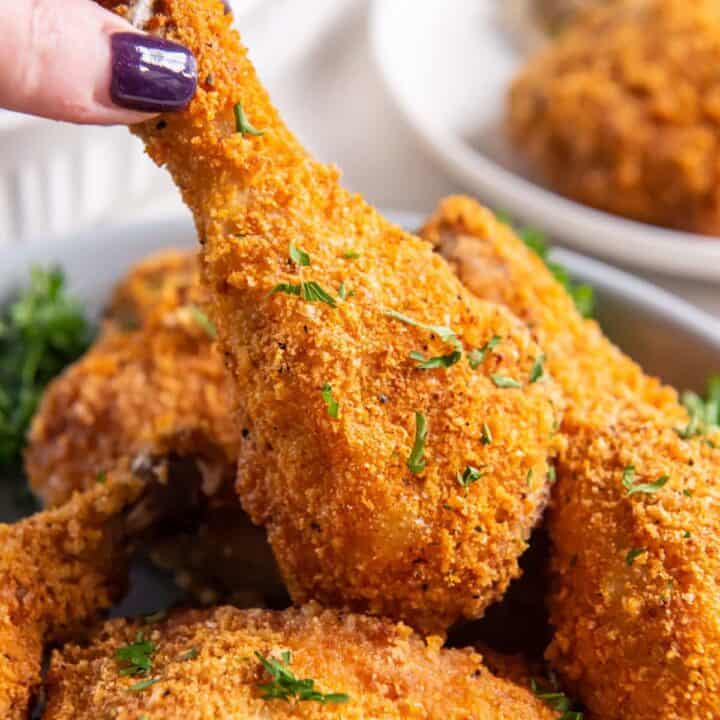 a feminine hand picking up a fried chicken leg from a platter of keto fried chicken pieces