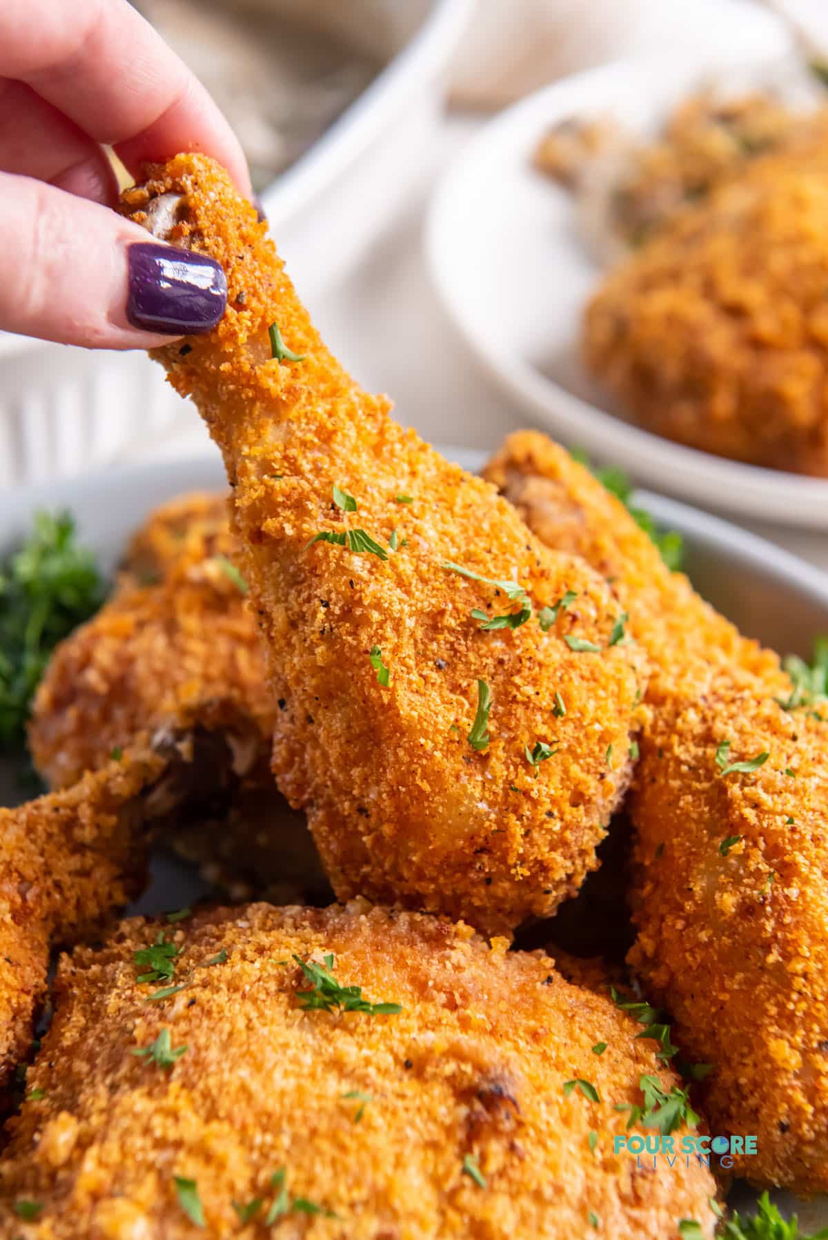 a feminine hand picking up a fried chicken leg from a platter of keto fried chicken pieces