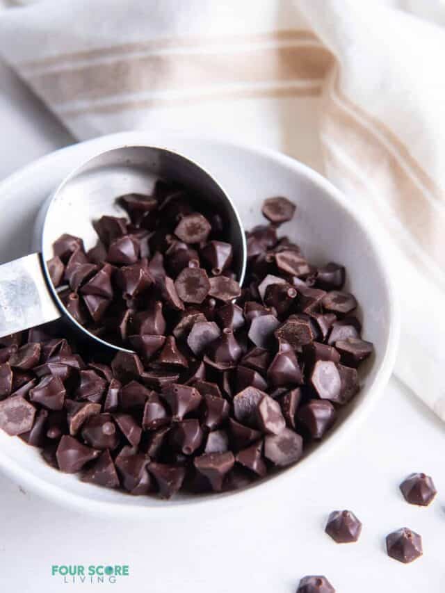 A small bowl of angular dark chocolate chips scooped with a small silver measuring cup.