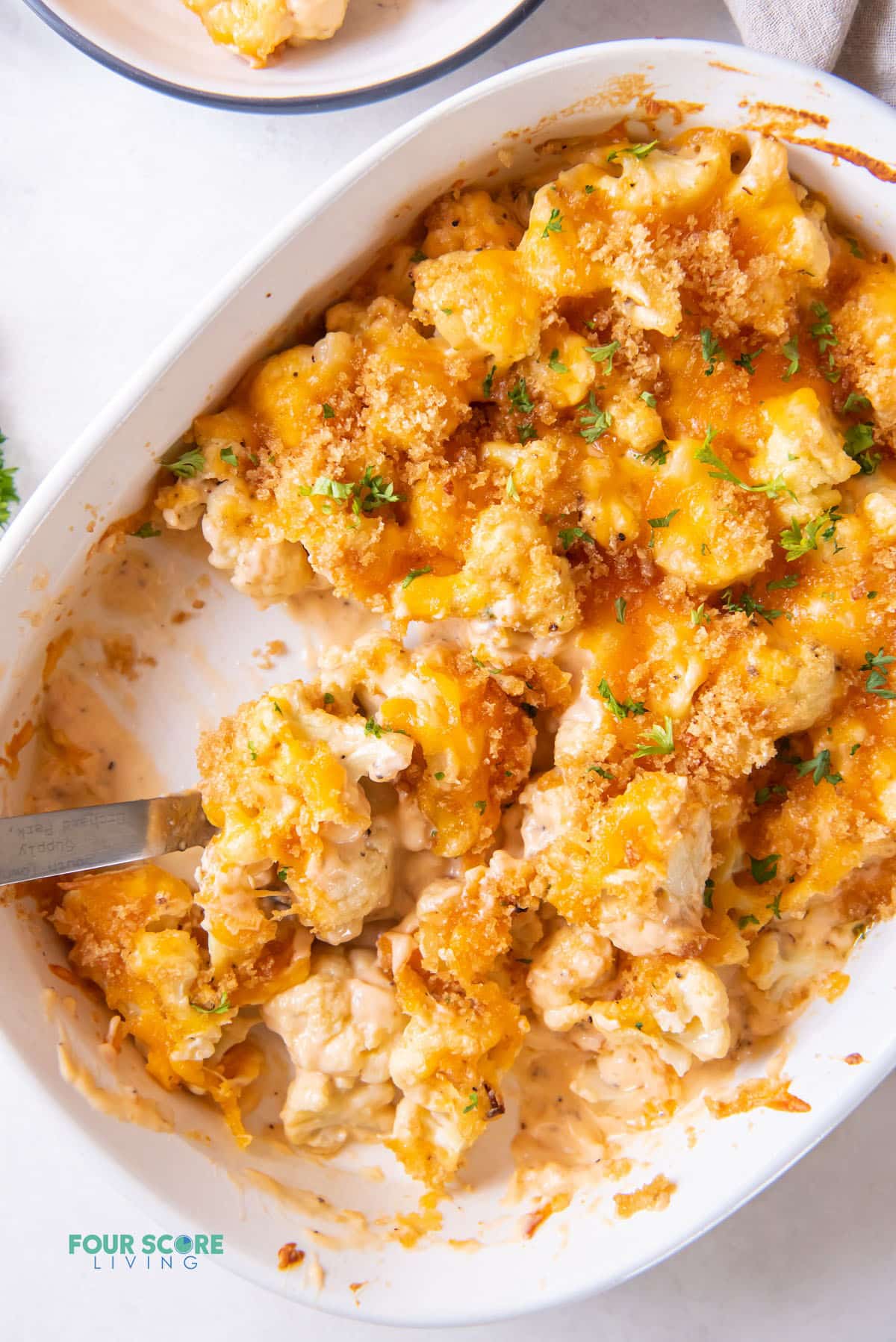 an oval casserole dish filled with keto cauliflower mac and cheese that has had a serving removed.