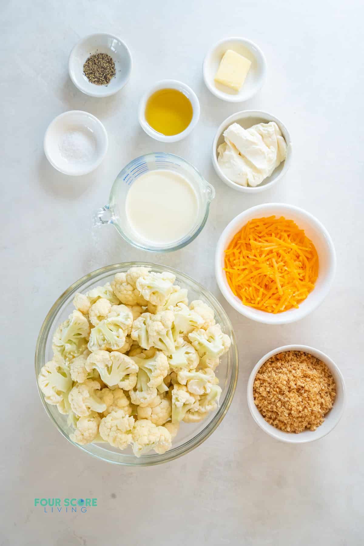 a bowl of cauliflower florets with all of the ingredients needed to make cauliflower mac and cheese, measured into bowls, viewed from above.