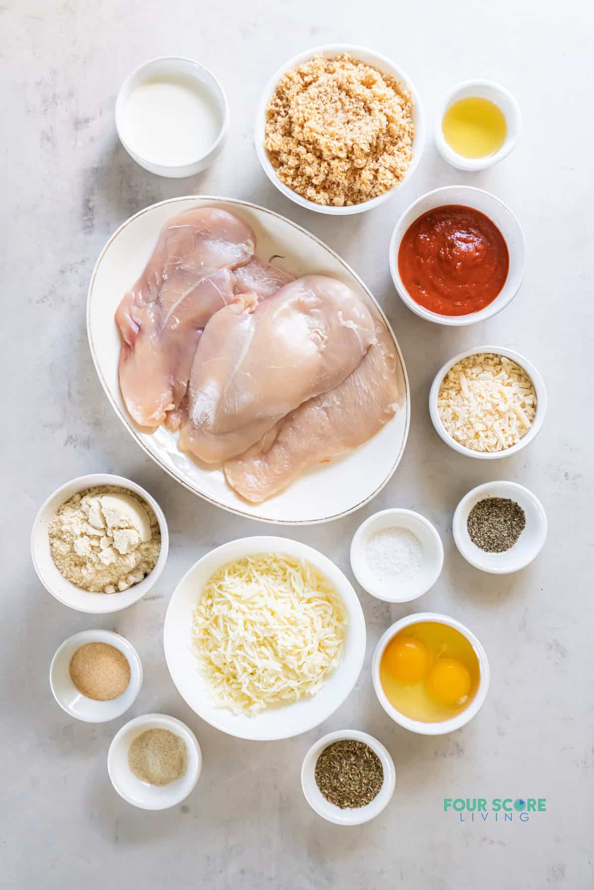 All of the ingredients you need to make keto chicken parmesan with chicken breasts. Each ingredient is measured into a bowl, and arranged on a counter, viewed from above