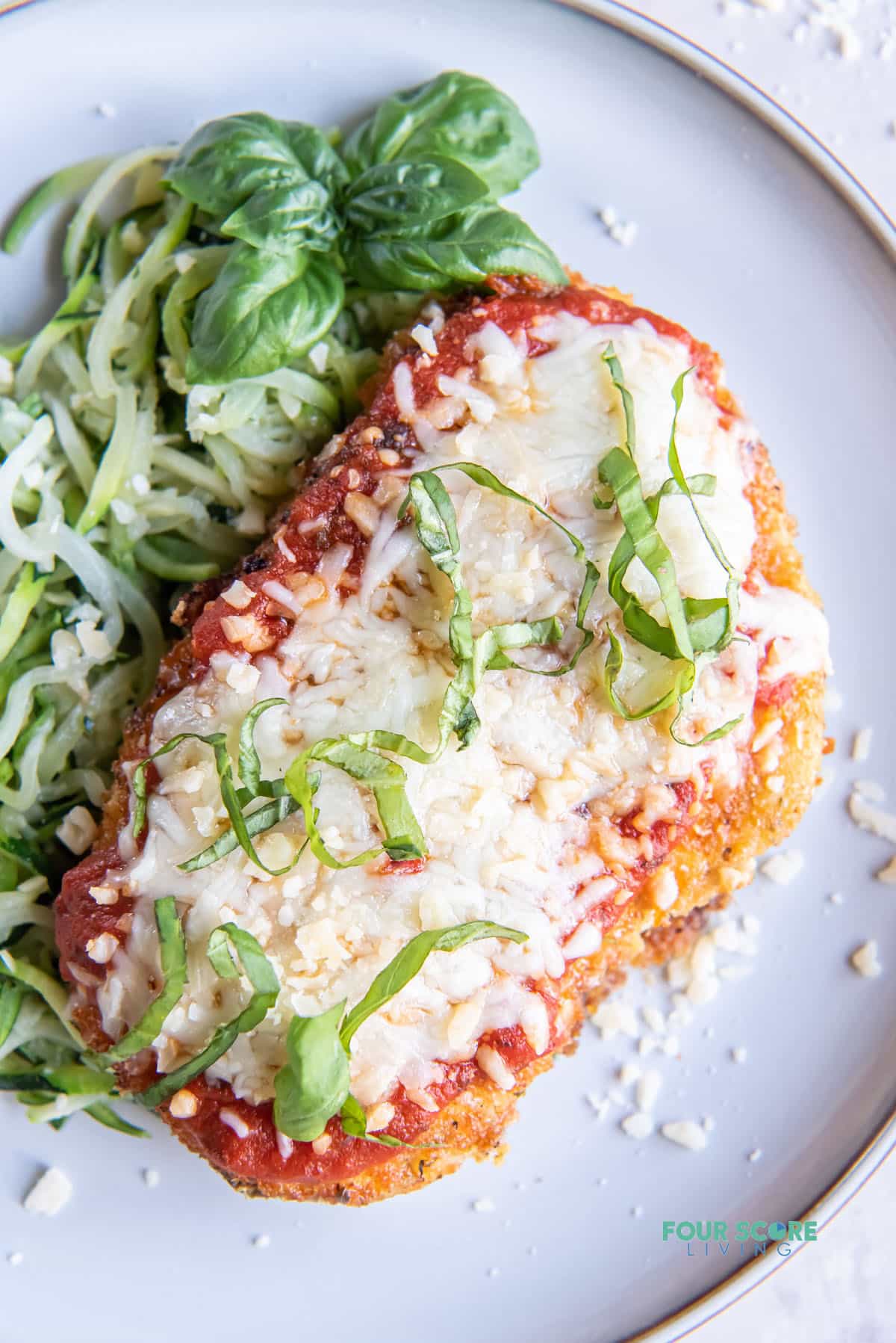 a keto chicken parmesan cutlet garnished with cut basil leaves, with a size of zoodles