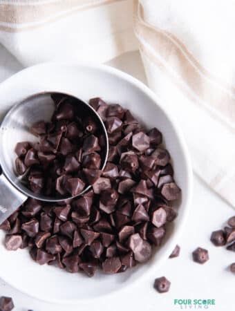 a bowl of homemade keto chocolate chips scooped by a small silver measuring cup, viewed from above