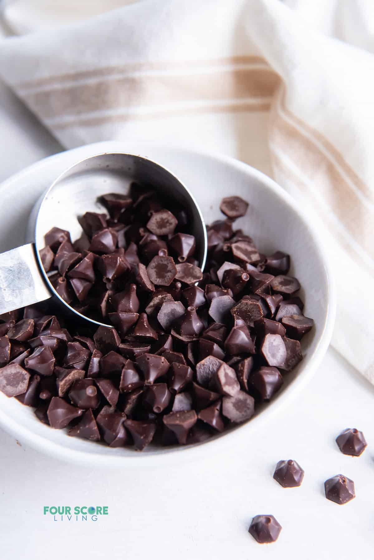 a small bowl of angular dark chocolate chips scooped with a small silver measuring cup.