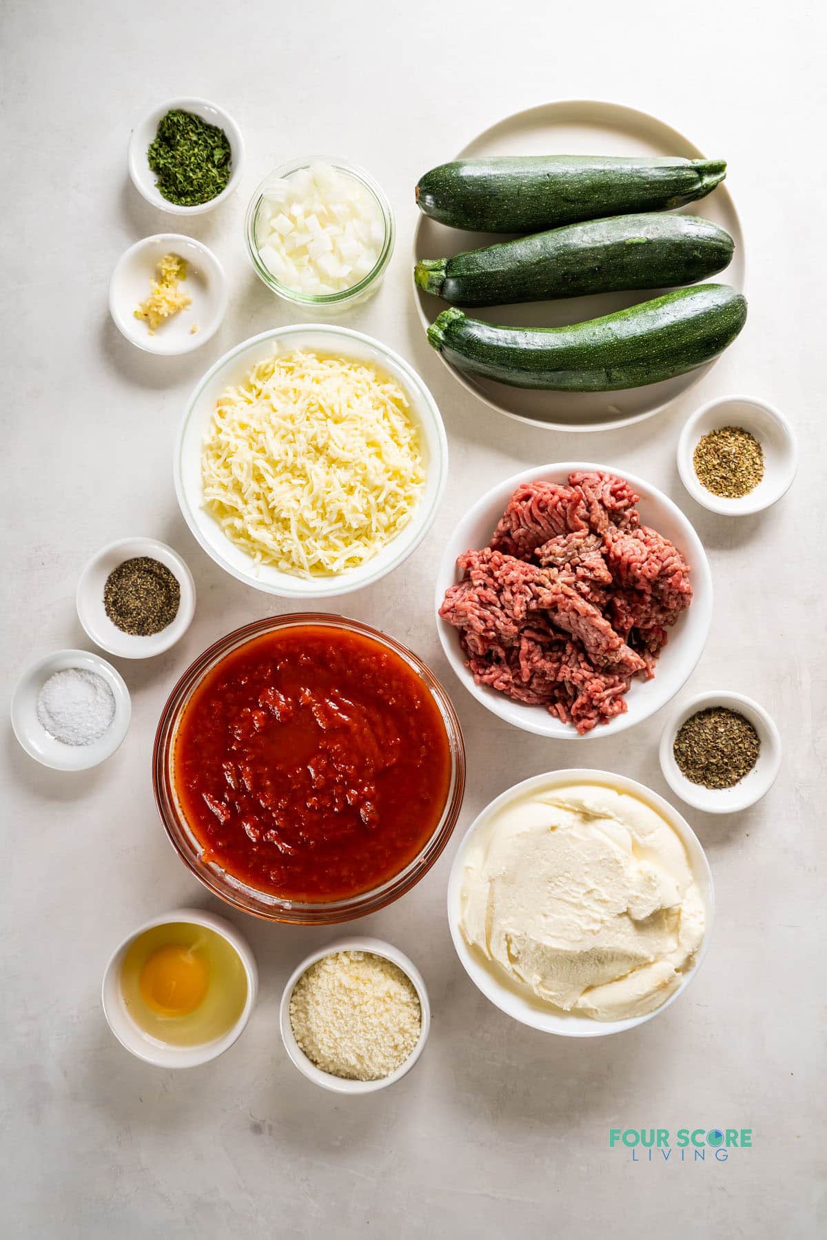 The ingredients needed to make a keto lasagana with zucchini, all measured into small bowls and viewed from overhead