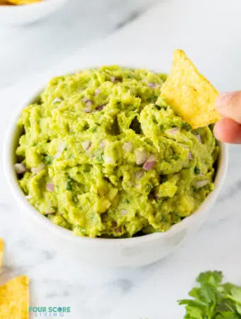a hand dipping a tortilla chip into 4 ingredient guacamole