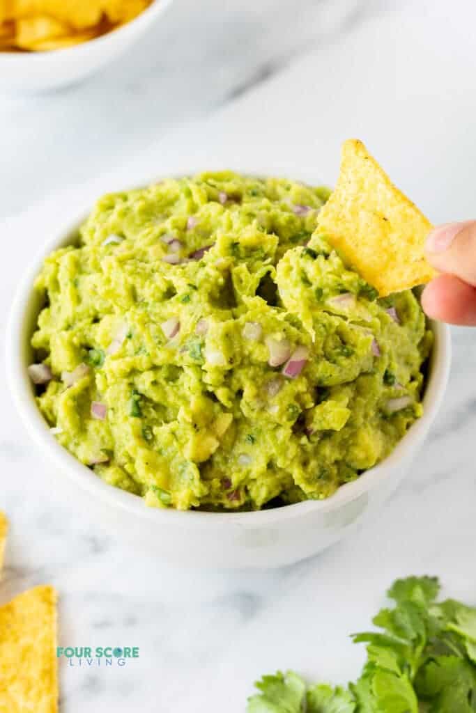 a hand dipping a tortilla chip into 4 ingredient guacamole