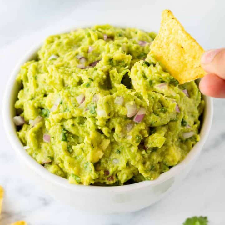 a hand dipping a tortilla chip into 4 ingredient guacamole