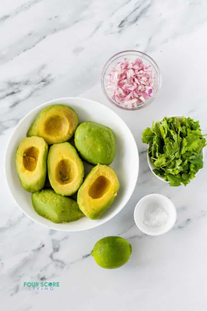 the ingredients in 4 ingredient guacamole in separate bowls including avocados, red onion, cilantro, salt, and lime