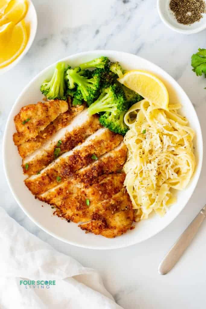 topview of plate of chicken fritta with fettucine and steamed broccoli