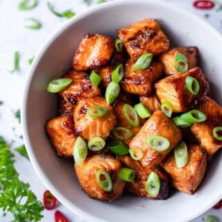 picture of salmon bites in a white bowl with chopped scallions scattered on top