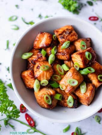 picture of salmon bites in a white bowl with chopped scallions scattered on top