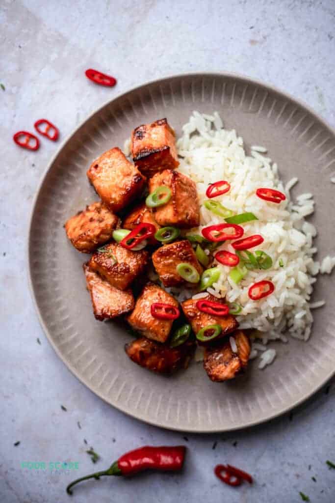 photo of finish salmon bites recipe on a plate next to rice with scallions and red peppers scattered on top