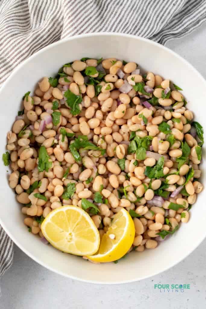 top view photo of white bean recipe in a white bowl with two lemon wedges, and a stripped kitchen towel above the bowl