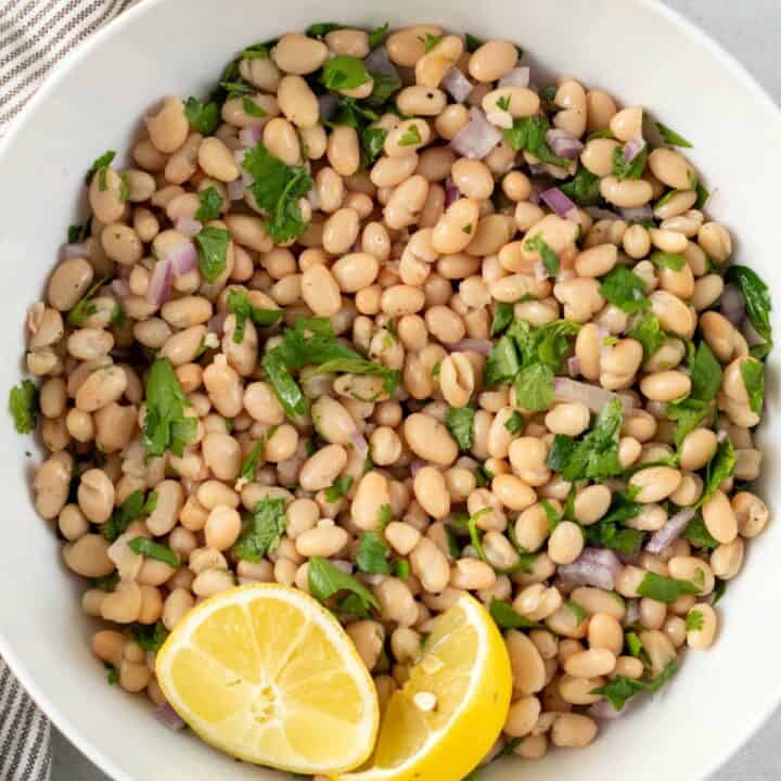 top view photo of white bean recipe in a white bowl with two lemon wedges, and a stripped kitchen towel above the bowl