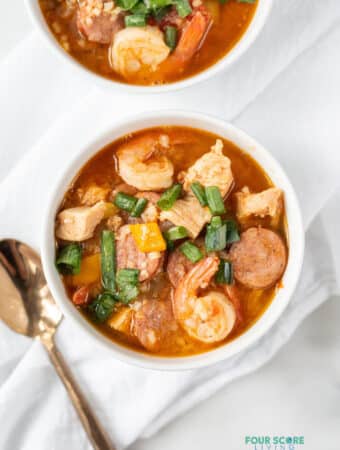 Topview photo of Keto Gumbo in two white bowls, ready to eat. They are sitting on white kitchen towels with a gold spoon next to the bowl.