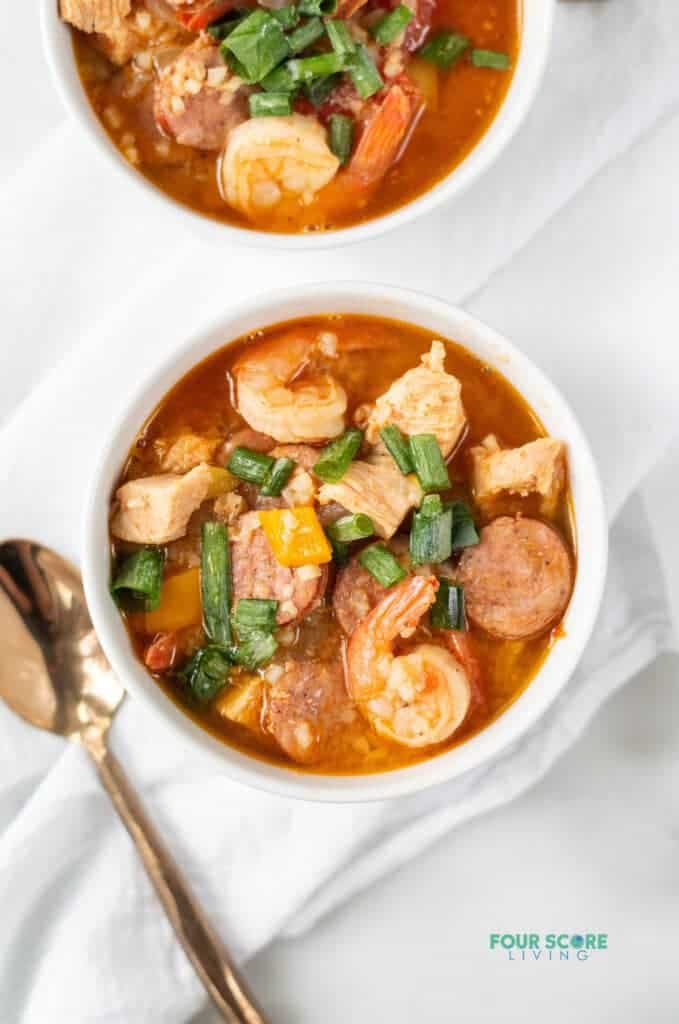 Topview photo of Keto Gumbo in two white bowls, ready to eat. They are sitting on white kitchen towels with a gold spoon next to the bowl.