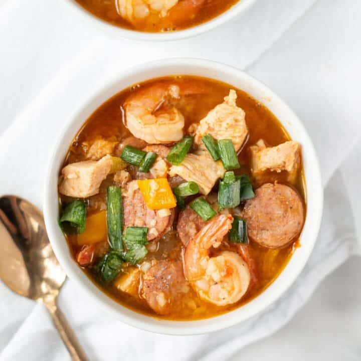 Topview photo of Keto Gumbo in two white bowls, ready to eat. They are sitting on white kitchen towels with a gold spoon next to the bowl.