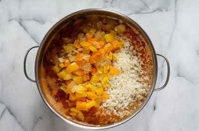 Topview photo of Keto Gumbo with cauliflower rice, bell peppers, and chopped onions added to the stockpot.