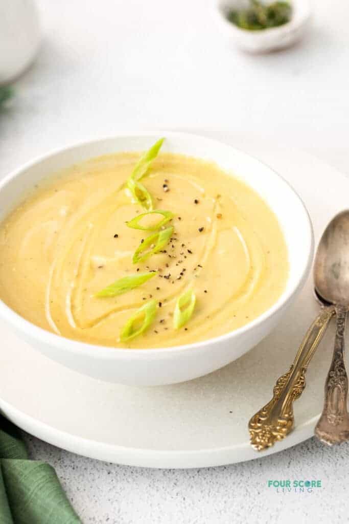 Photo of Magic Leek Soup in a white bowl, on a white plate. There are two silver spoons on the plate.