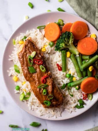 Top view photo of Peanut Butter Glazed Salmon over rice with steamed veggies in a white bowl.