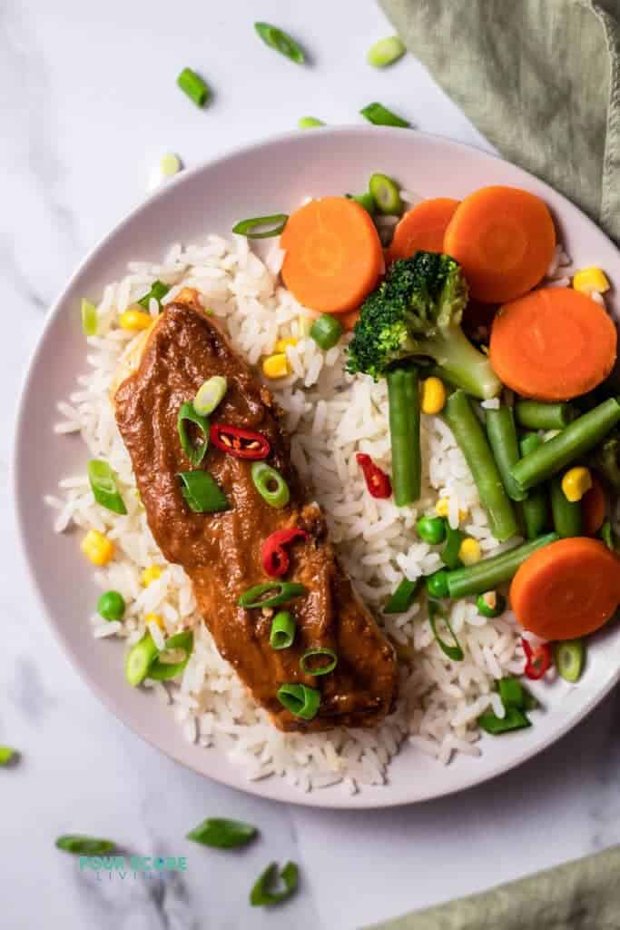 Top view photo of Peanut Butter Glazed Salmon over rice with steamed veggies in a white bowl. 