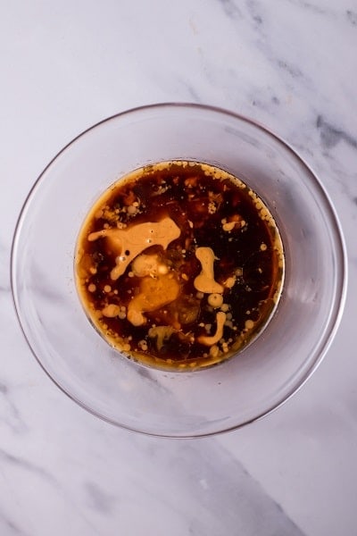 Top view photo of peanut butter, lemon juice, soy sauce, ginger, rice wine vinegar, and sesame oil in a clear bowl, ready to mix together.