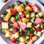 top view photo of pineapple salad in a white bowl, with strawberries and a kitchen towel above the bowl and flowers below it