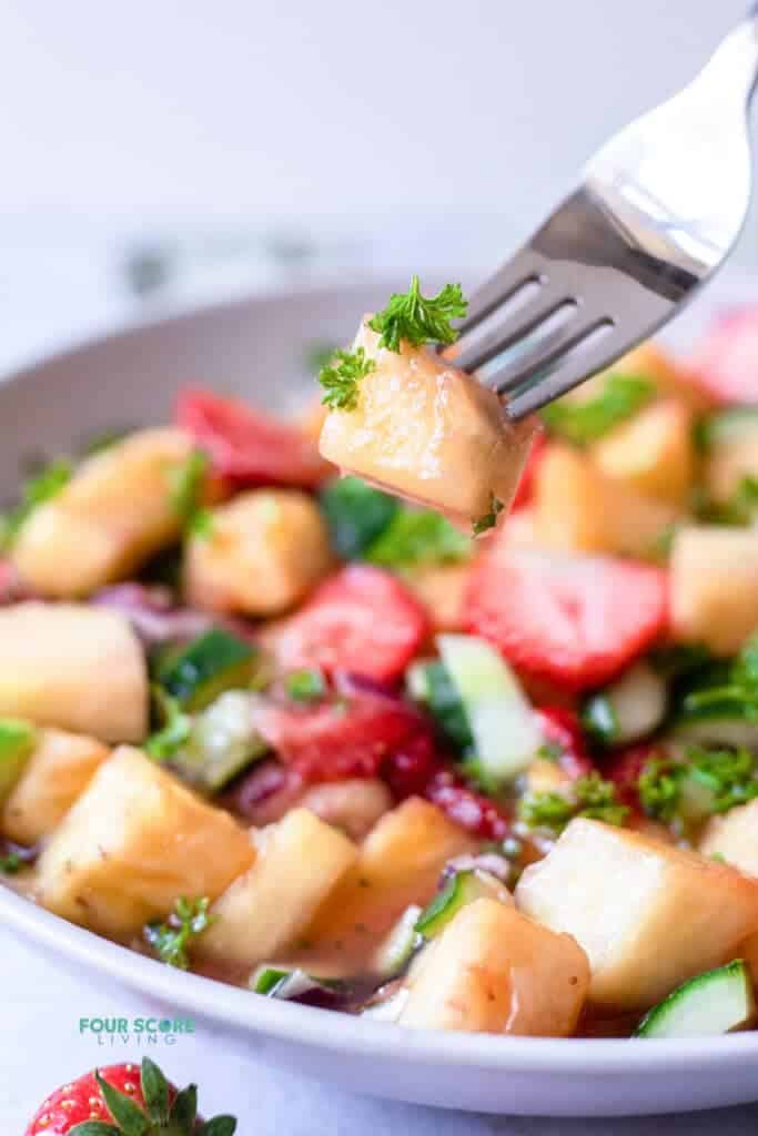 closeup photo of a fork picking up a pineapple slice from a bowl of pineapple salad