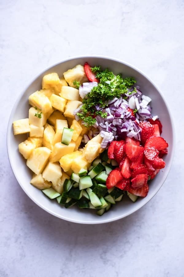 top view photo of ingredients to make pineapple salad in a white bowl, ready to be mixed