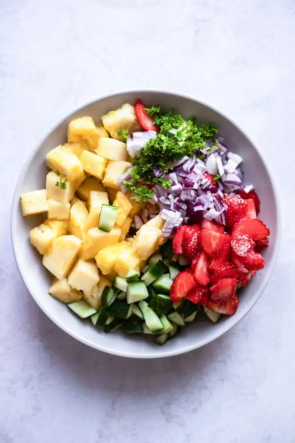 top view photo of ingredients to make pineapple salad in a white bowl, ready to be mixed