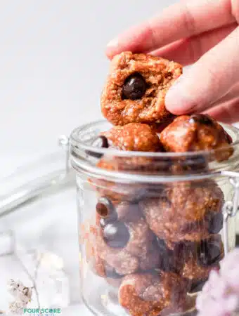 closeup photo of a hand grabbing a protein cookie dough ball with a bite taken out of it, in a glass jar.