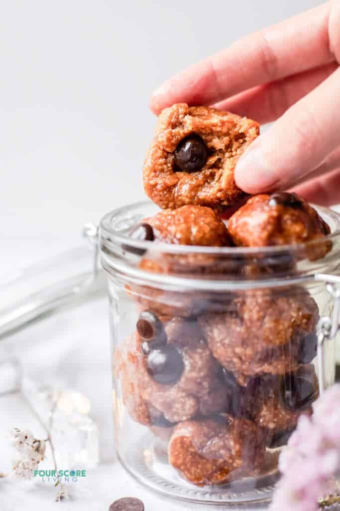 closeup photo of a hand grabbing a protein cookie dough ball with a bite taken out of it, in a glass jar.