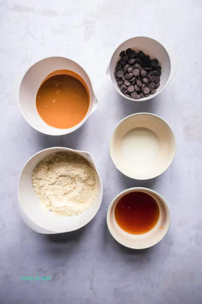 top view photo of ingredients to make protein cookie dough, in separate white bowls.
