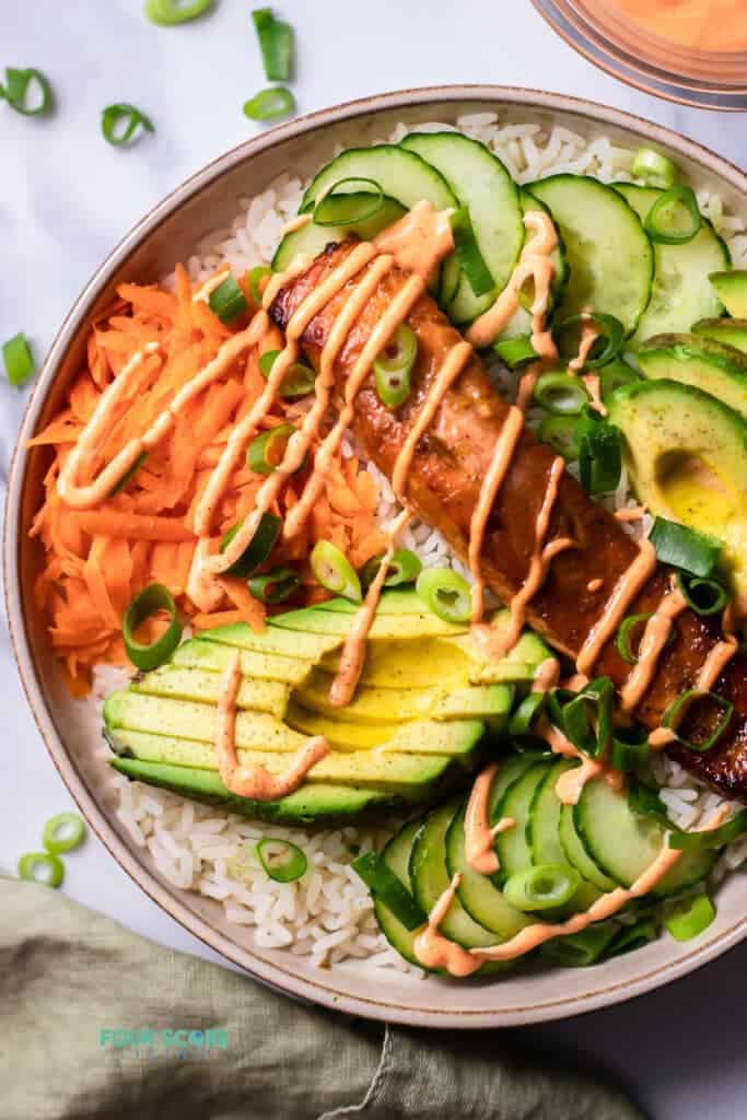 Top view photo of Salmon Rice Bowl, in a bowl and ready to serve. There is a kitchen towel next to the bowl. 