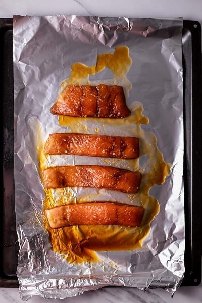Top view photo of salmon on a baking sheet lined with tin foil, cooked and ready to add to Salmon Rice Bowls.