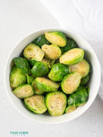 photo of a bowl of steamed brussels sprouts with salt and pepper on top, with a white kitchen towel next to the bowl
