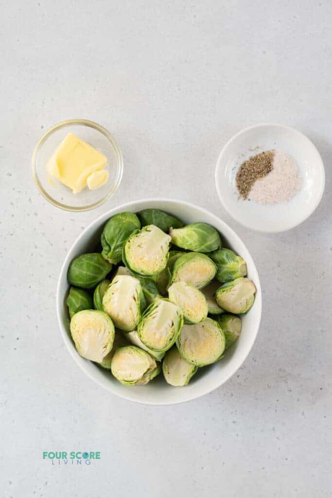 top view photo of ingredients to make steamed brussels sprouts in separate bowls, including brussels sprouts, butter, salt, and pepper