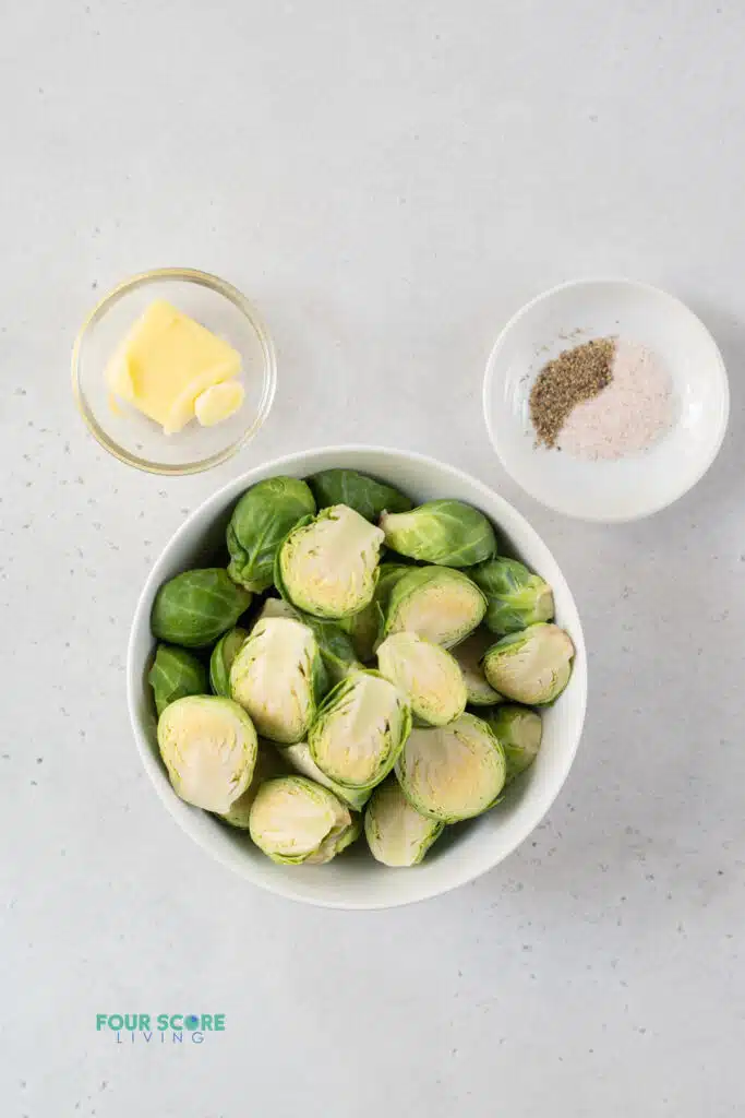 top view photo of ingredients to make steamed brussels sprouts in separate bowls, including brussels sprouts, butter, salt, and pepper