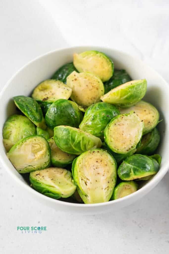 photo of a bowl of steamed brussels sprouts with salt and pepper on top, with a white kitchen towel next to the bowl