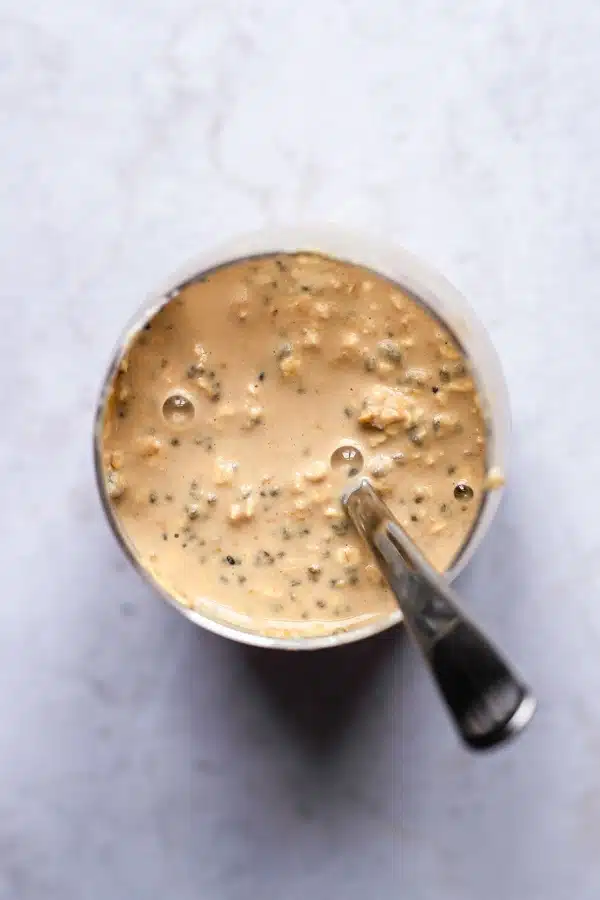 top view photo of a glass container with oats, chia seeds, milk, coffee, mascarpone, maple syrup, and vanilla extract inside, all mixed together