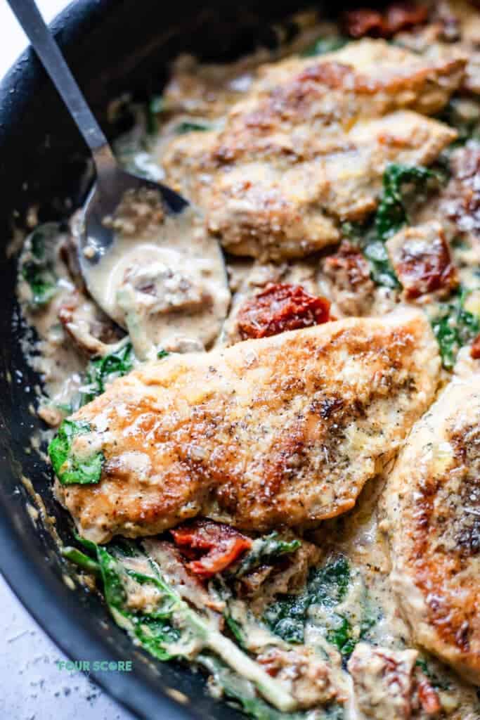 closeup photo of tuscan chicken in a cast iron skillet with a silver spoon dipped in, ready to serve